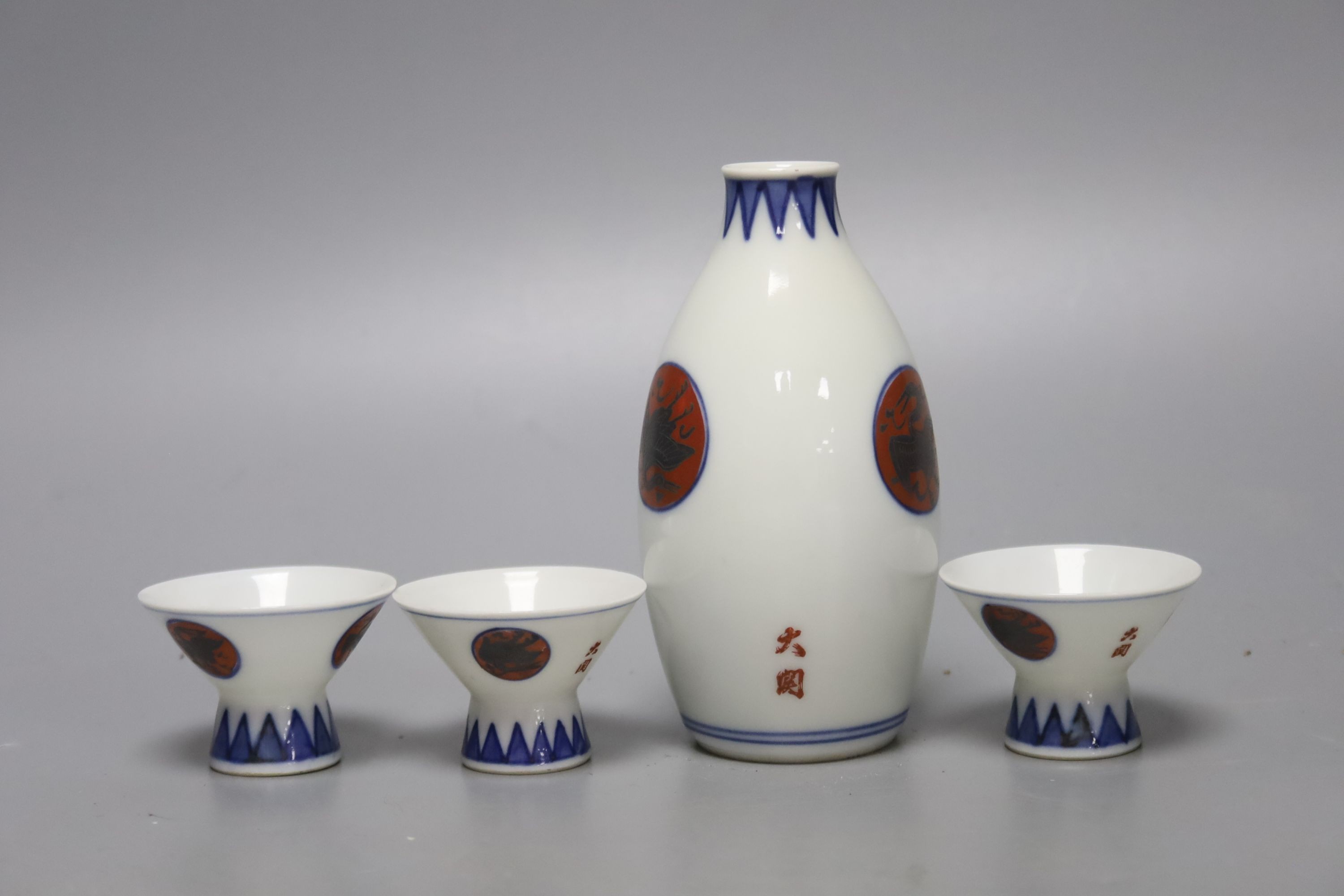 A Japanese blue and white porcelain sake flask, with associated cups, height 12cm